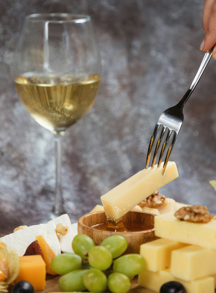 Ein Stück Käse wird mit einer Gabel serviert – harmonische Kombination von Wein und Feinkost