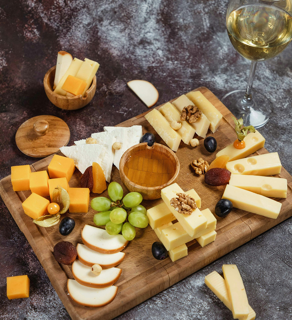 Vielfältige Käseplatte mit Trauben, Nüssen und einem Glas Weißwein – Delikatessen aus dem Wein-Markt Jansen